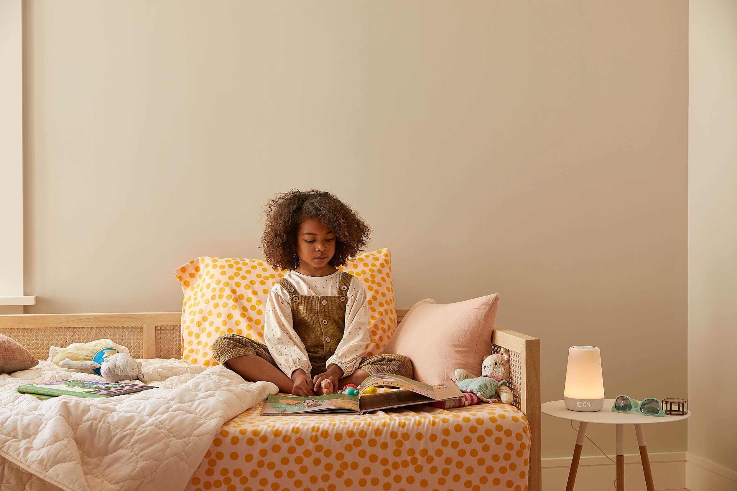 A kid reads next to an illuminated Hatch Rest sleep device
