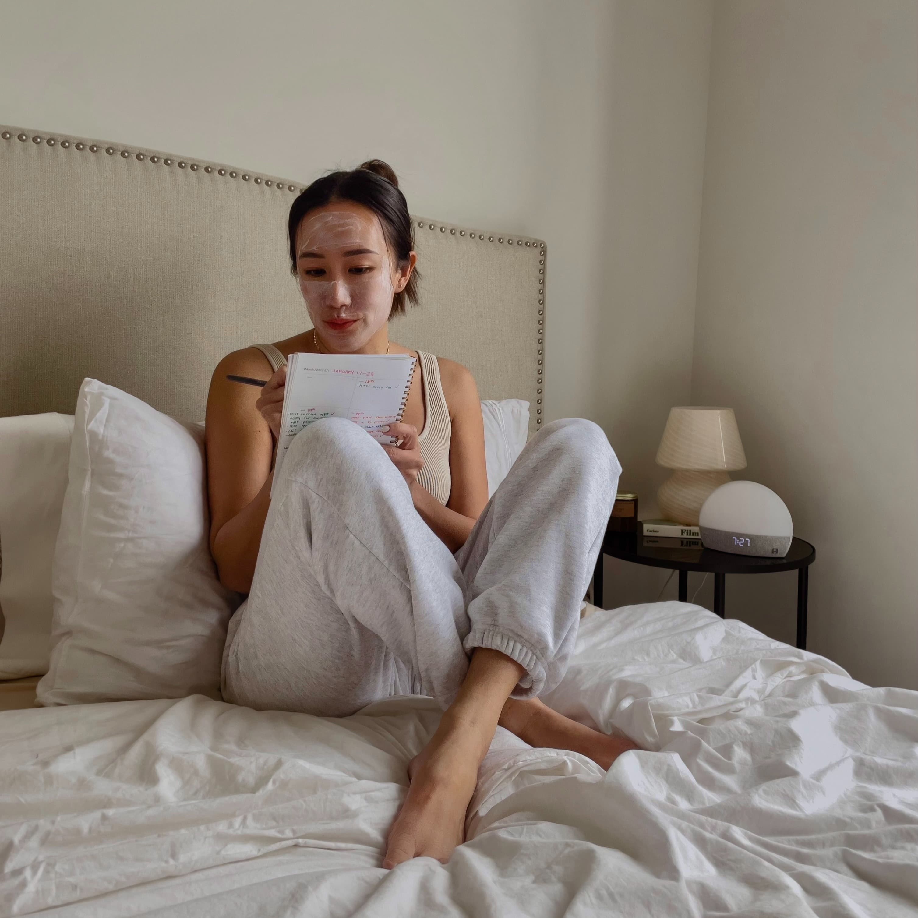 Woman in bed writing in her notebook with a facial mask