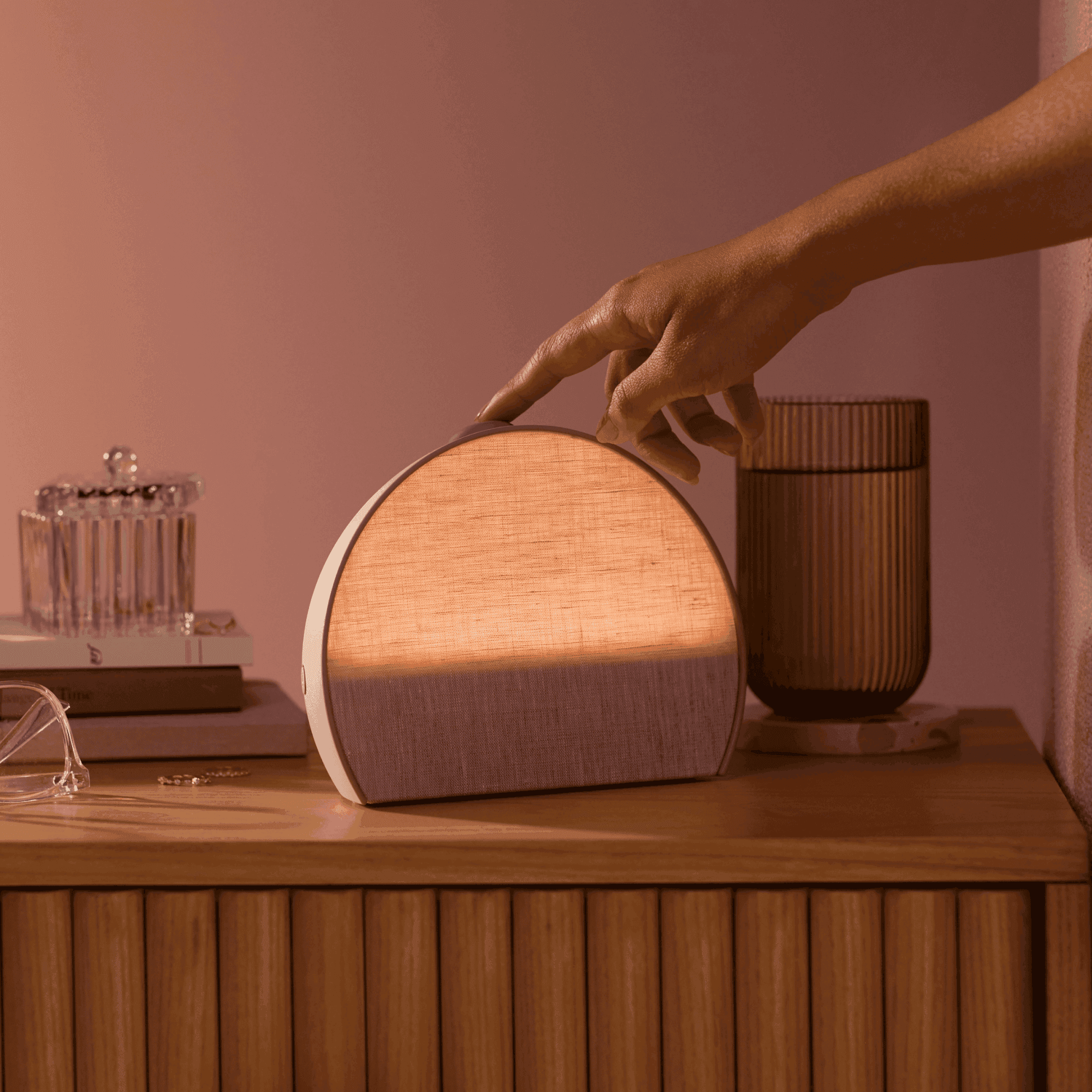 Restore 3 - Rosy colorway on a nightstand with a hand touching the top button