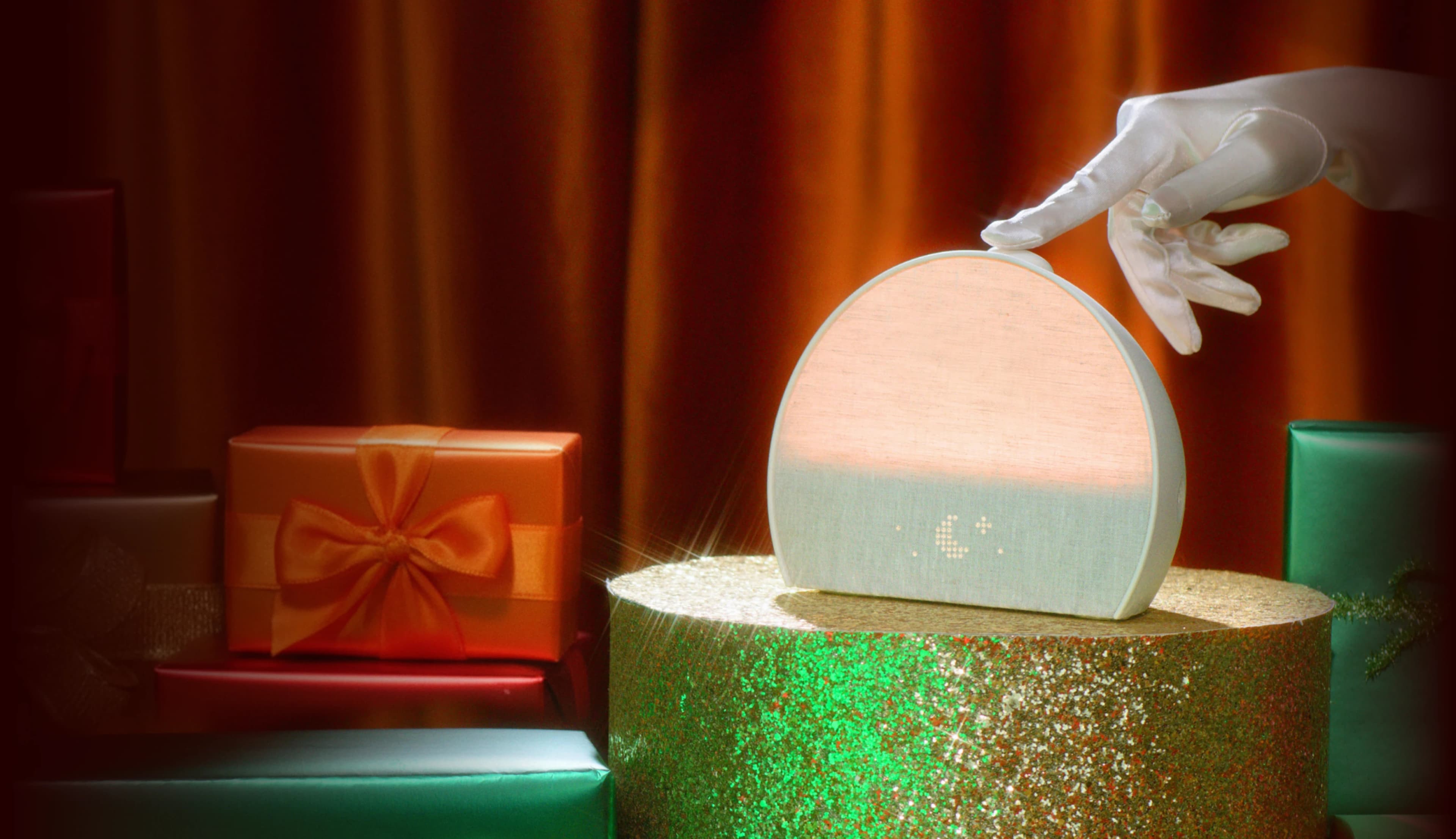 Hand tapping the top button on a Hatch Restore 3 with a holiday gift background