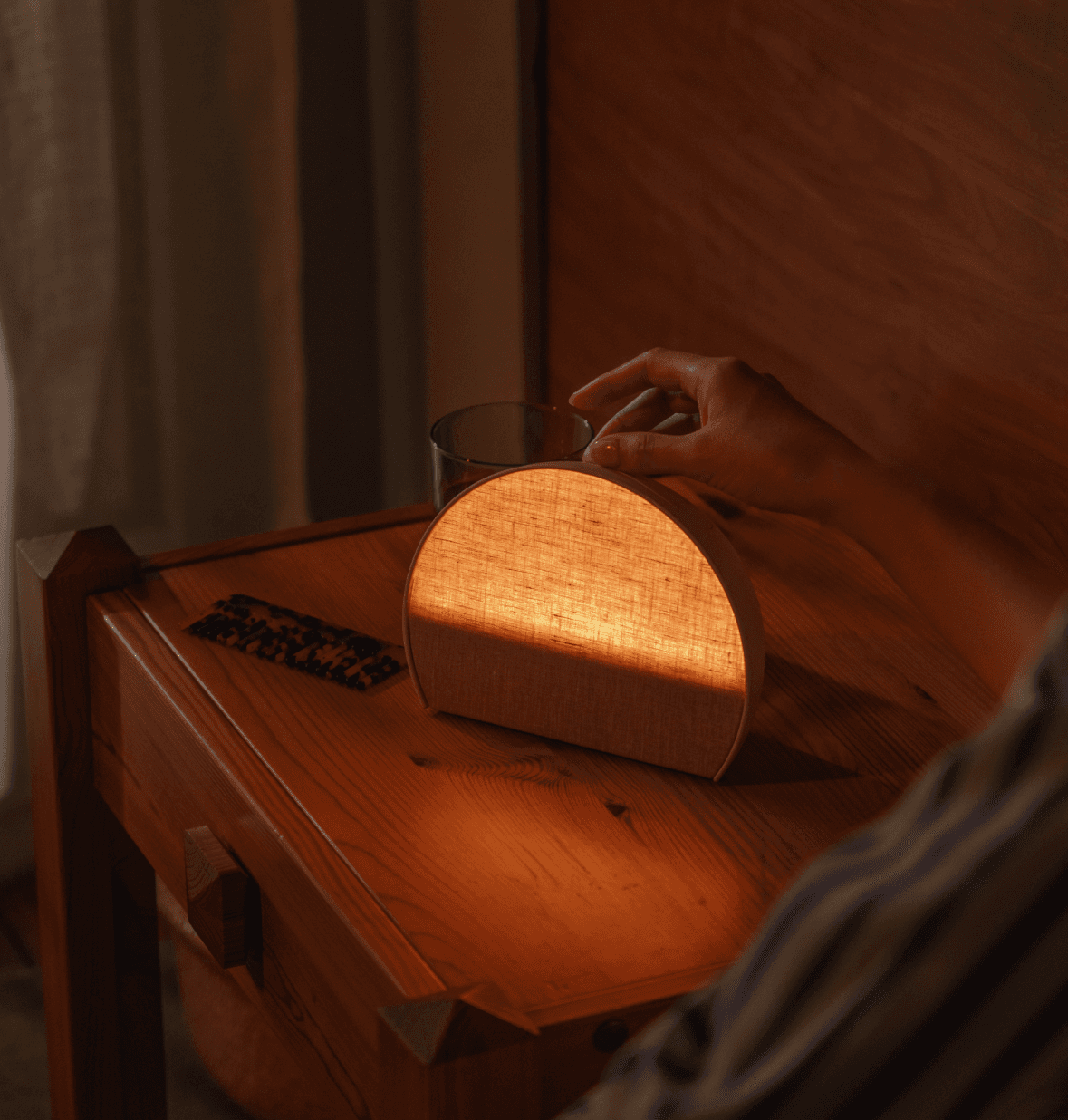 Person pressing top button of lit up Hatch sleep clock on nightstand