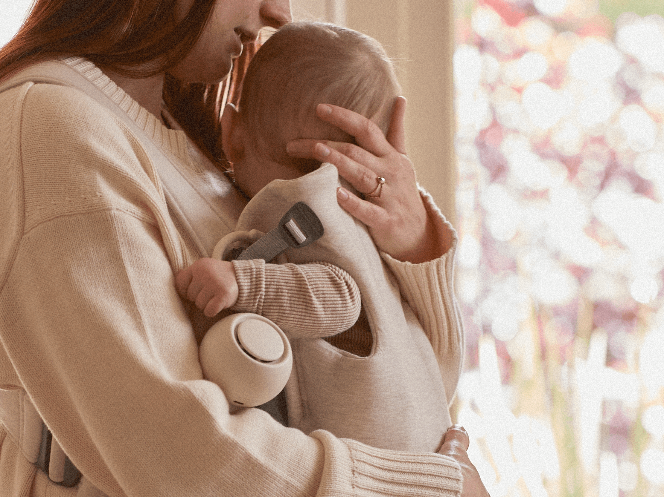 Mother cradling her baby with Hatch Go putty colorway clipped to the baby's carrier